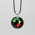 A round pendant necklace on a black cord, featuring a black background with a silhouette of Africa filled with the green, yellow, and red Rastafarian flag colors, set in a silver-toned bezel.