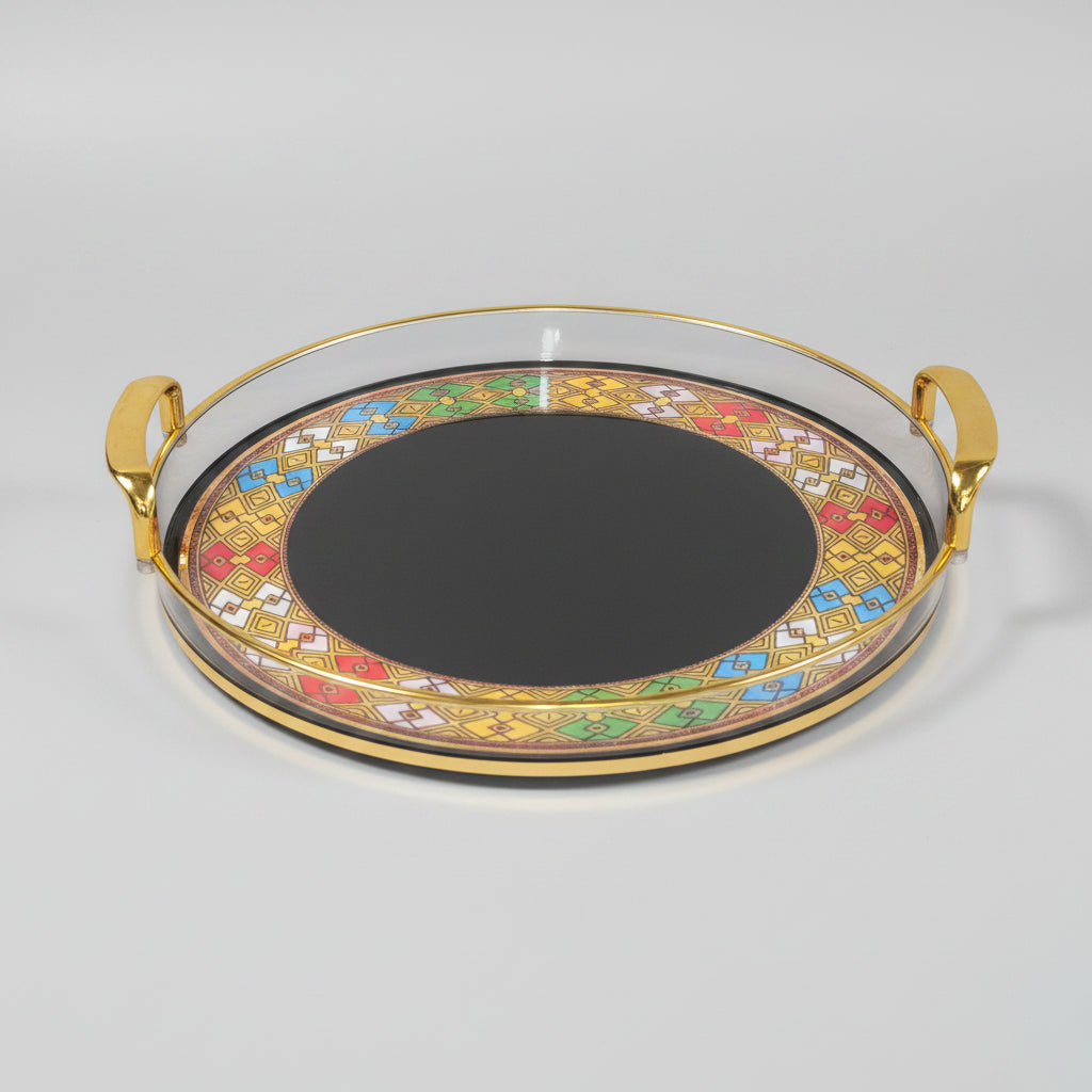 A round serving tray with gold handles and a colorful geometric border pattern, shown on a black marble surface.