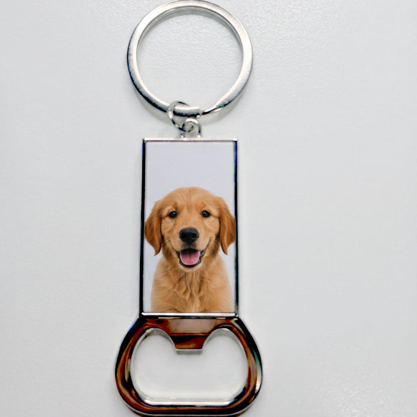 A silver metal bottle opener keychain with a white rectangular photo plate in the center containing placeholder text 'YOUR PHOTO HERE', shown on a light gray background.