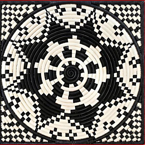 A square woven basket or mat featuring a bold black and off-white geometric spiral pattern with concentric rings and checkerboard sections, photographed straight-on against a dark background.