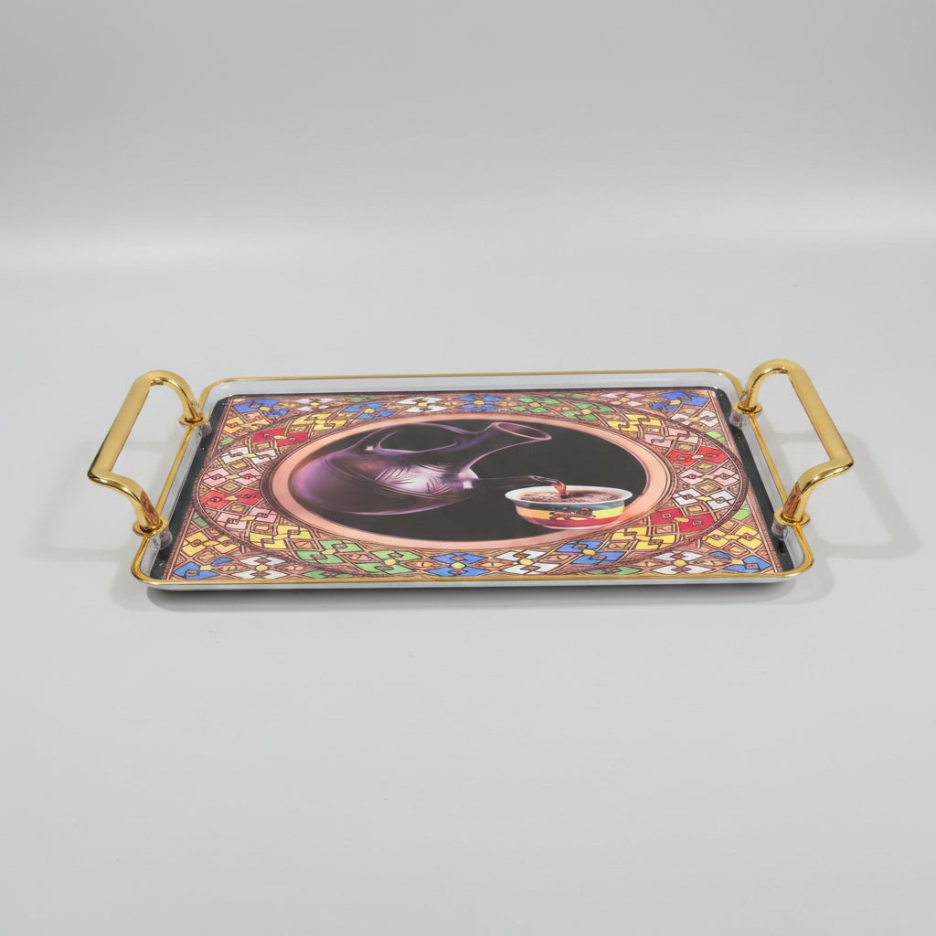 A rectangular decorative tray with gold-toned metal handles, featuring a colorful printed design of a dark purple pitcher pouring into a cup, set against a black marble background.