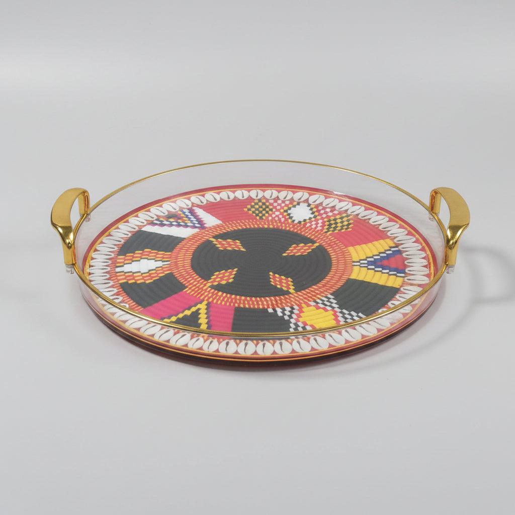 A round decorative serving tray with gold-tone metal handles, featuring a vibrant African-inspired geometric beadwork-style pattern in red, black, yellow, pink, white, and blue on a black marble surface.