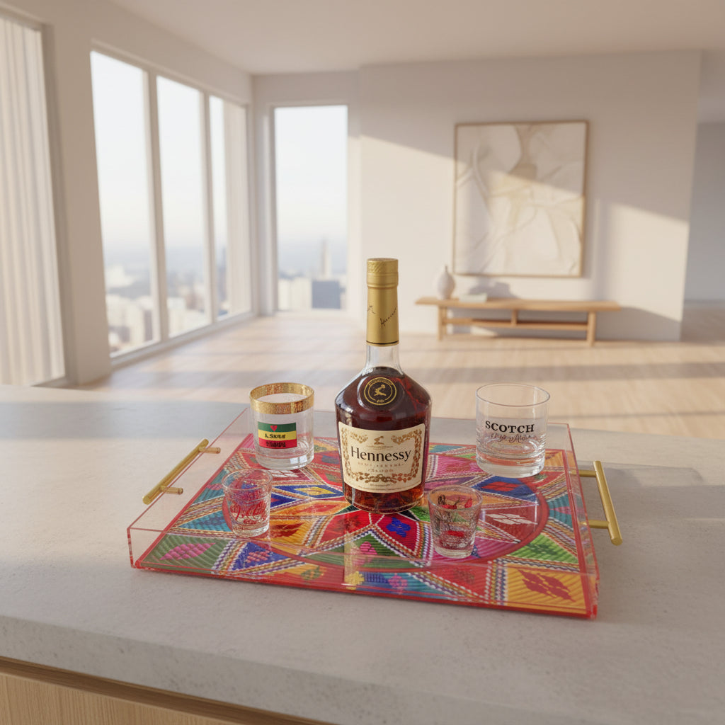 A rectangular acrylic serving tray with gold handles, decorated with a colorful geometric mandala pattern, styled on a black table with a bottle of Hennessy cognac and several glasses.
