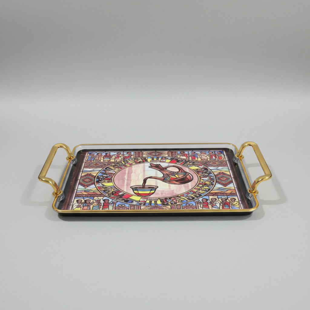 A rectangular decorative tray with gold-toned metal handles, featuring a colorful stained-glass-style illustration of figures and a central pitcher pouring into a cup, placed on a black marble surface.