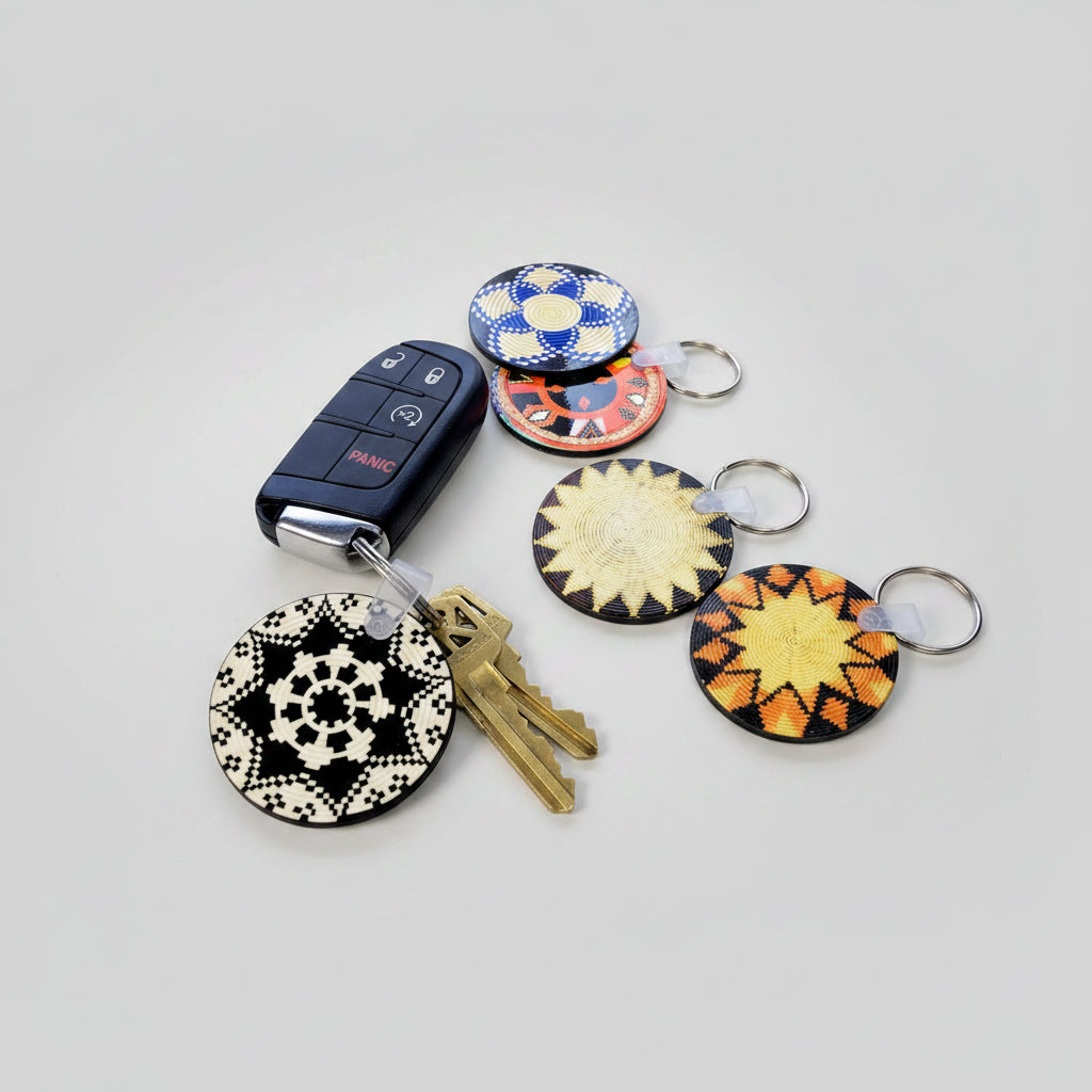 Several round keychain magnets with geometric patterns are arranged on a wooden surface, including one attached to a black car key fob and a set of keys. The keychains feature black, white, blue, orange, yellow, and red patterns.