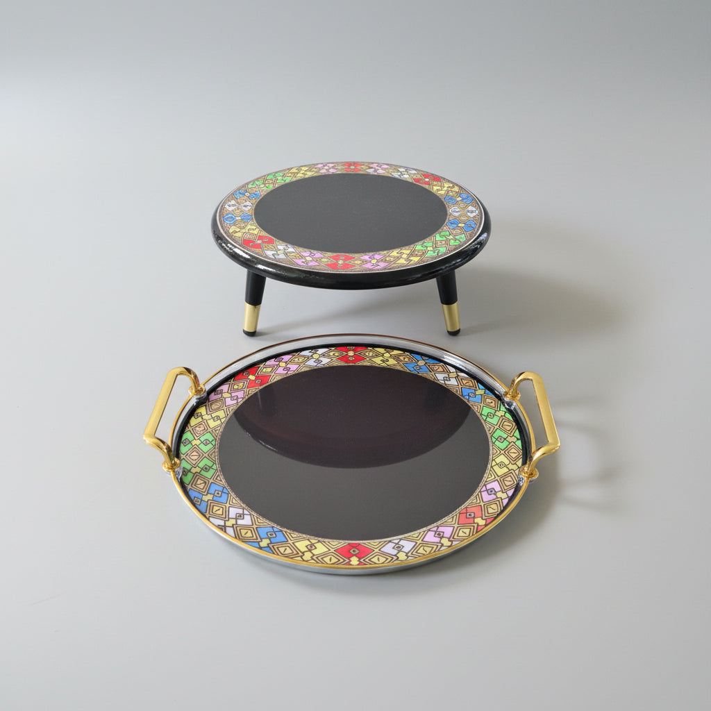 Two round black serving trays with colorful geometric borders and gold-toned handles, displayed on a black marble surface.