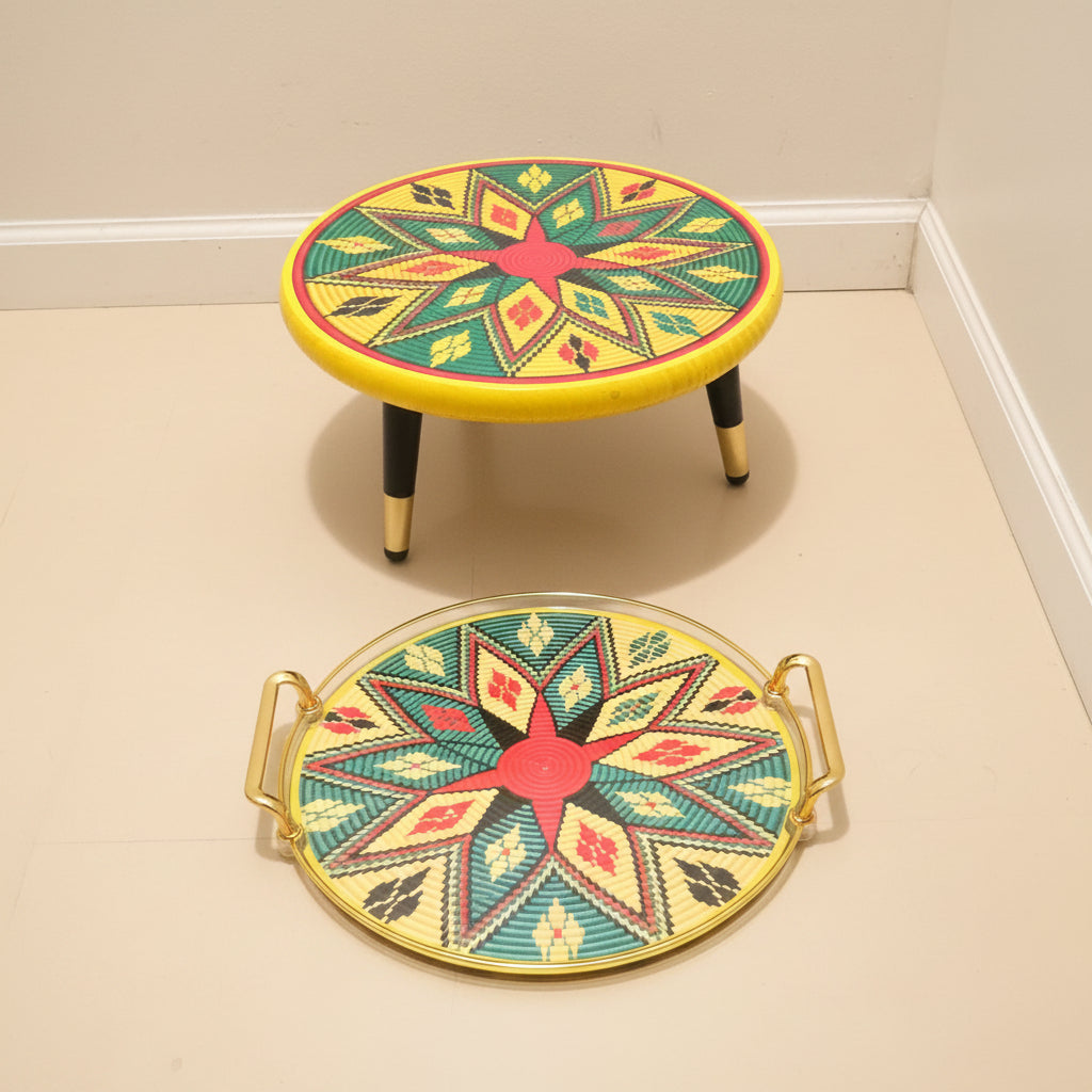 A set of two round decorative trays with gold handles, featuring a colorful geometric star pattern in yellow, green, red, and black on a wood-look floor against a white wall.