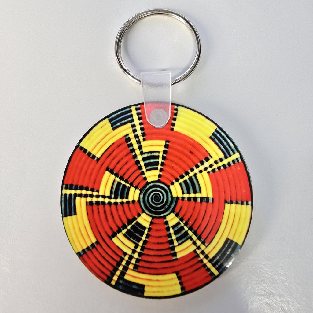 A circular woven keychain with a vibrant red, yellow, and black geometric pattern, attached to a silver metal key ring on a light gray background.