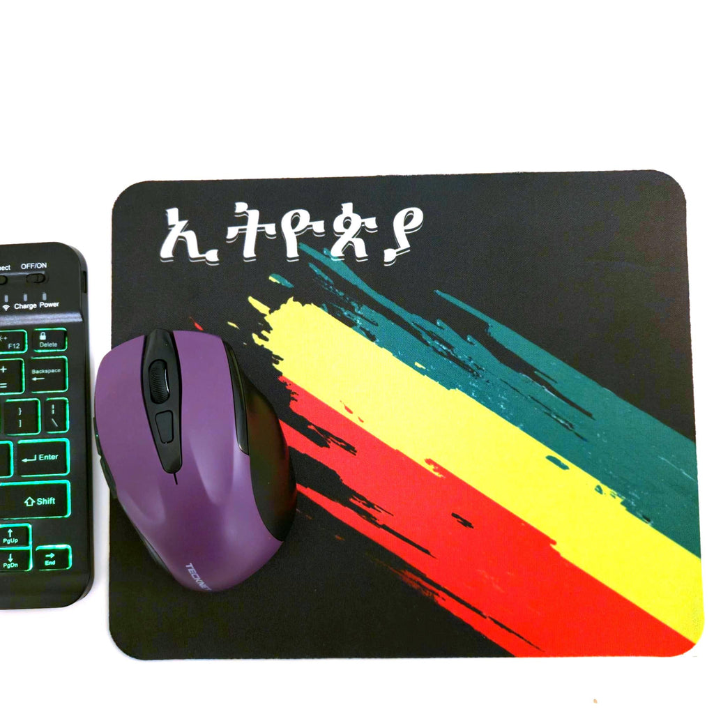 A black rectangular mouse pad with a colorful diagonal brushstroke design in yellow, green, red, and orange, plus stylized white lettering near the top. A purple computer mouse rests on the pad.
