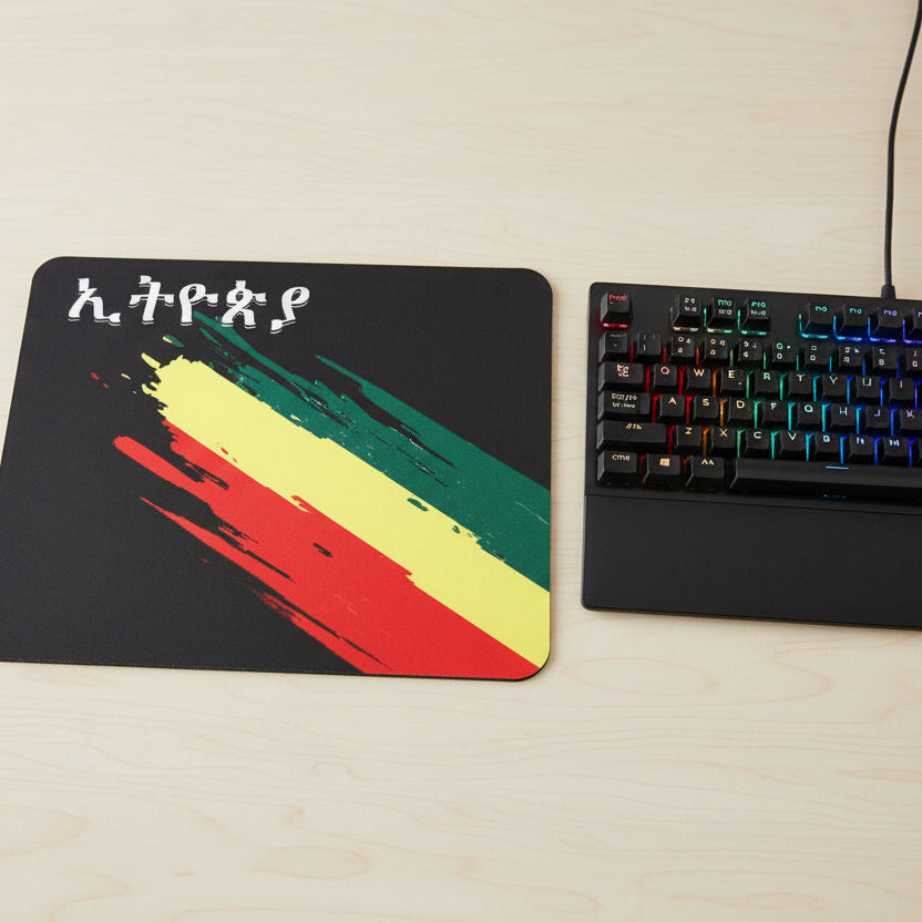 A black rectangular mouse pad with rounded corners, featuring a colorful diagonal brushstroke pattern in green, yellow, and red, along with stylized white characters in the top left. A purple and black computer mouse rests on the pad against a plain white background.