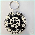 A round keychain featuring a black and white geometric pixelated pattern, attached to a silver split ring with a clear plastic connector, shown on a light gray background.