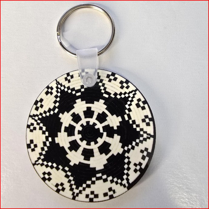 A round keychain featuring a black and white geometric pixelated pattern, attached to a silver split ring with a clear plastic connector, shown on a light gray background.