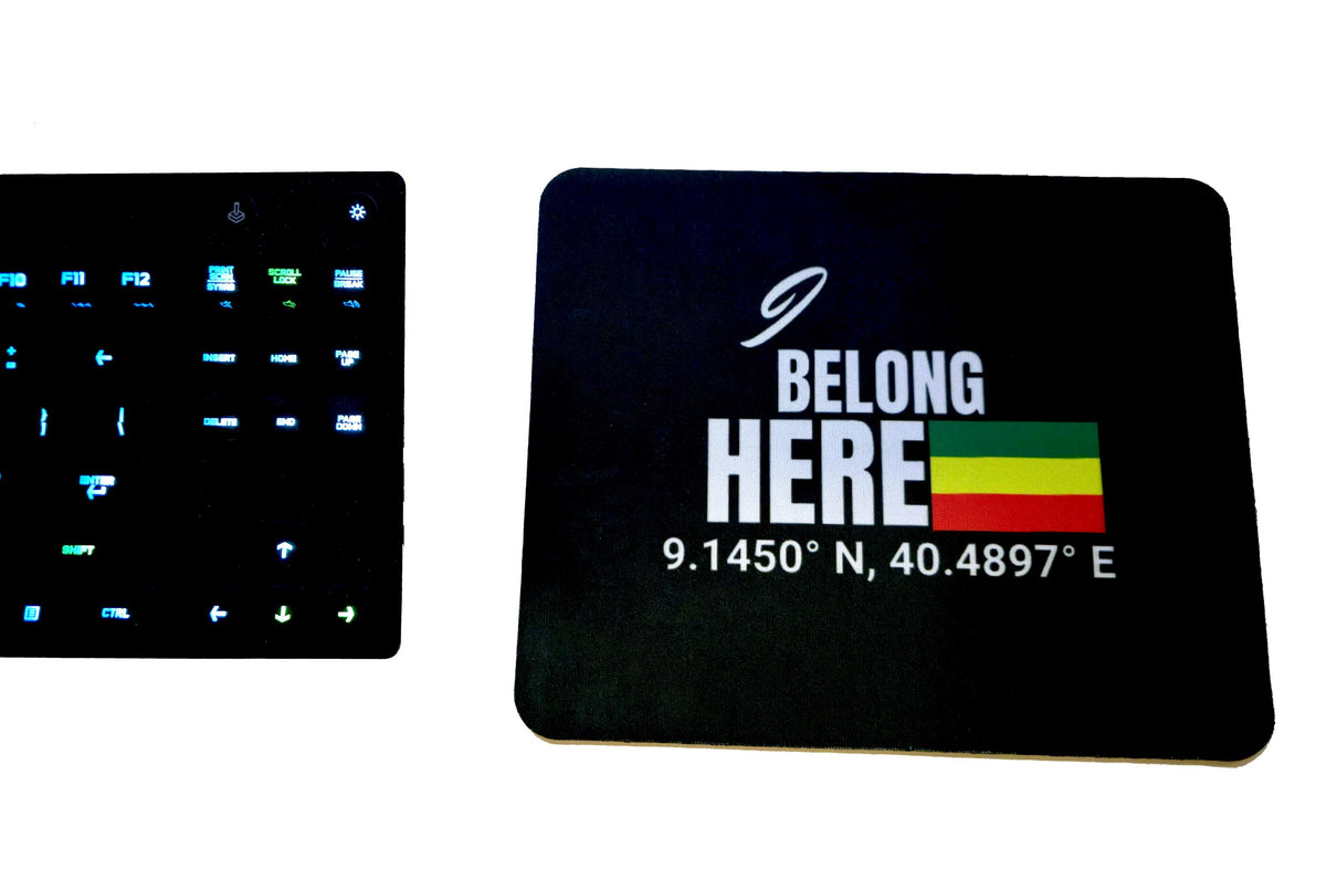 Two black rectangular items on a white background: a smaller square item on the left with a grid of blue icons and a larger rounded-corner rectangle on the right printed with the words 'BELONG HERE' and coordinates next to a small green, yellow, and red flag graphic.